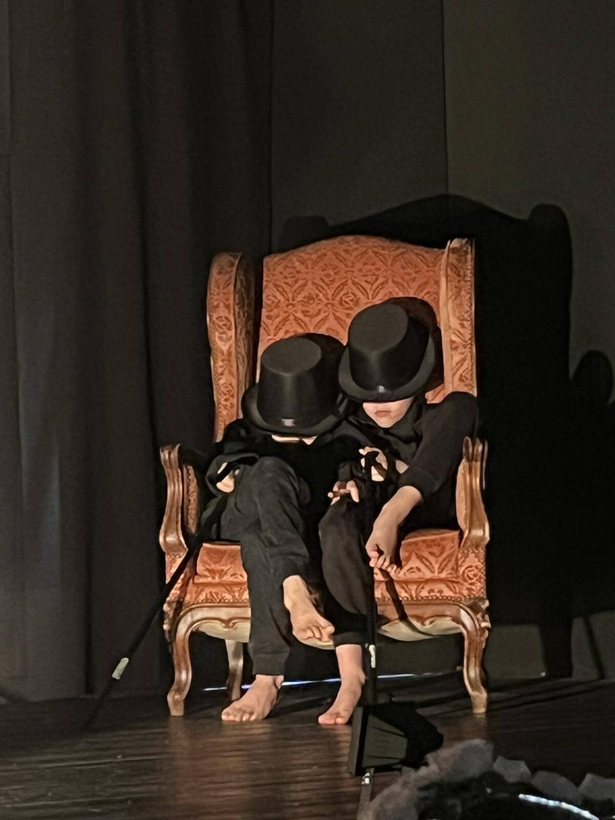 deux enfants assis sur un fauteuil, leurs visages sont cachés avec des chapeaux haut de forme